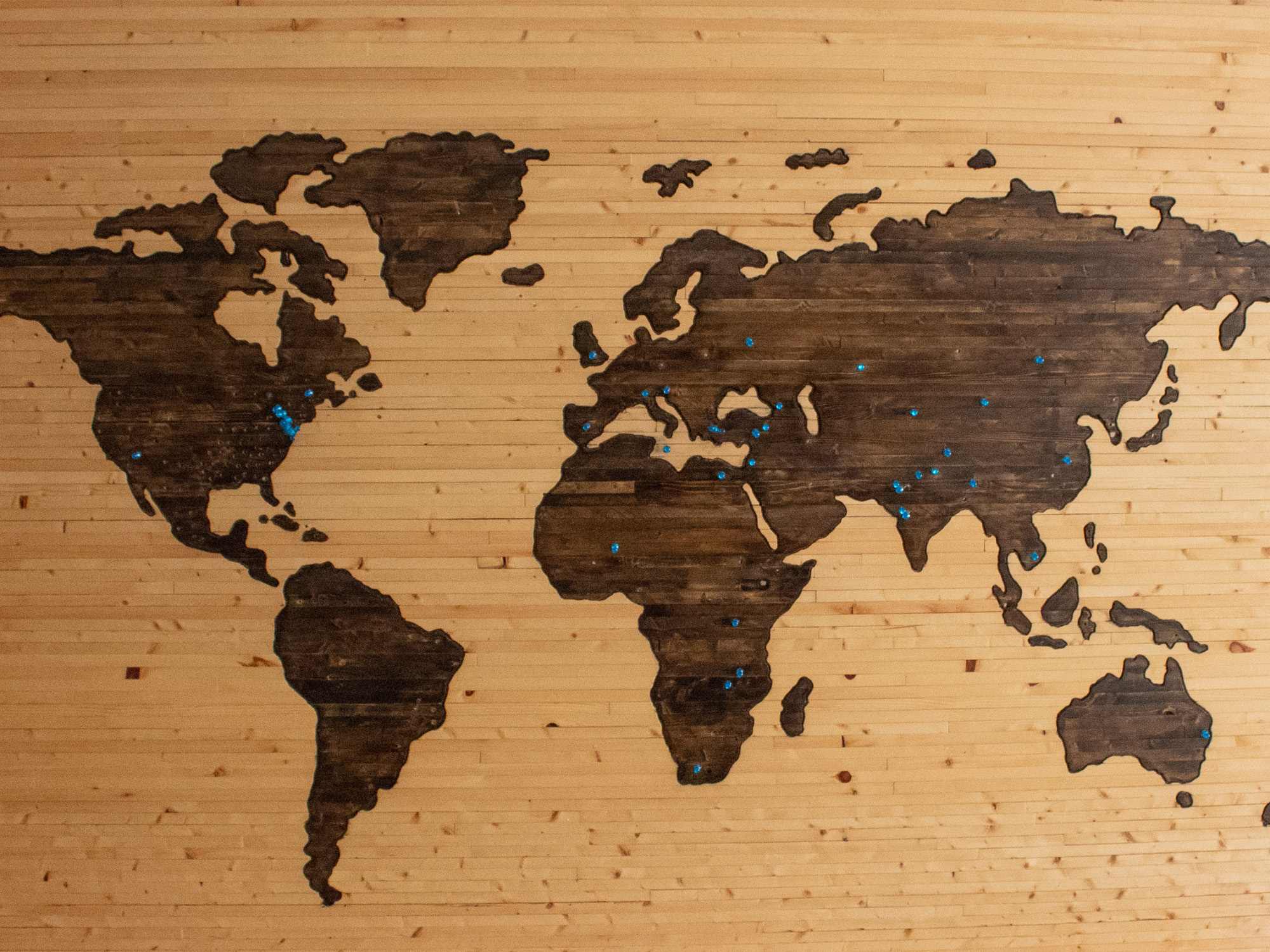 A map embossed onto a piece of wood in tones of tan and chocolate with blue pins dotting the continents